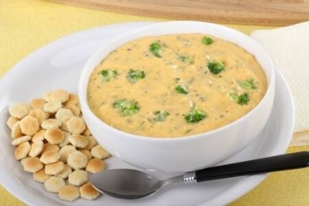 A bowl of broccoli cheese soup with a side of oyster crackers.